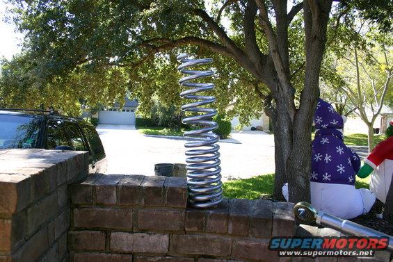 Silver coil spring on brick wall with trees and a black SUV in the background