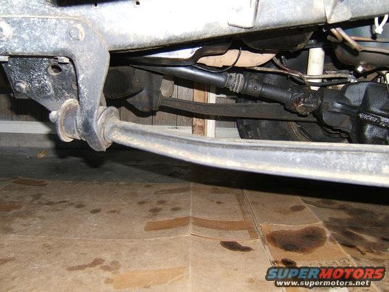 Underside view of a vehicle's suspension and drivetrain components, with oil stains on the floor below