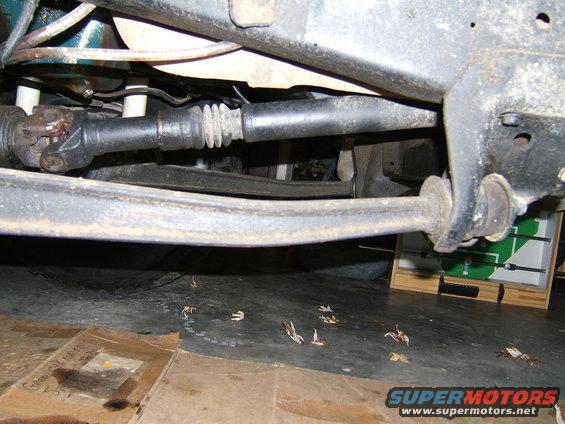 Underside view of a vehicle's driveshaft and suspension, showing rust and dirt