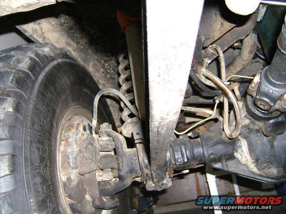 Undercarriage view of a vehicle's front suspension and drivetrain components, including a tire