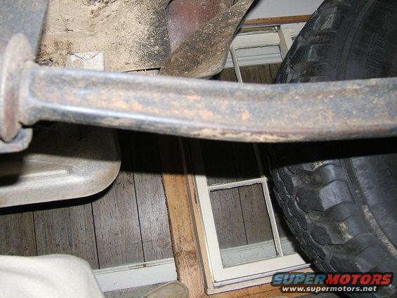Underside of a vehicle with exhaust pipe and tire visible, against a wood-paneled wall