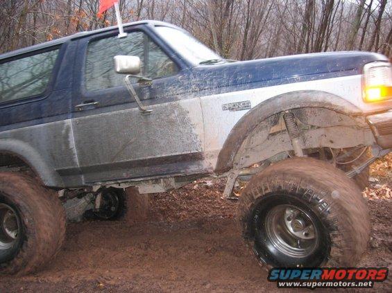 1995 Ford Bronco driving through mud with a red flag on top