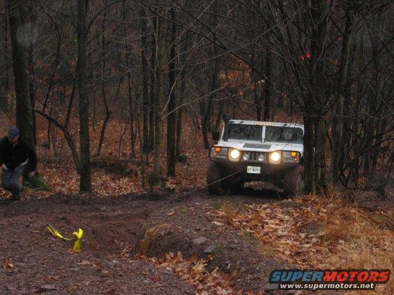 White SUV with a winch cable attached, driving on a muddy forest trail