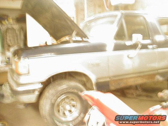 1987 Ford Bronco with hood open, front 3/4 view, showing damage and rust