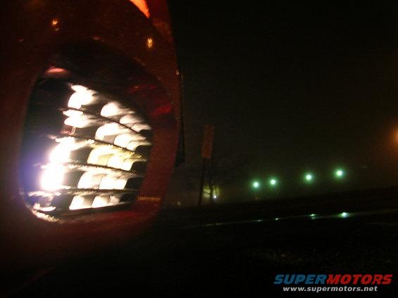 Close-up of a car's front grille with lights on, seen at night in fog