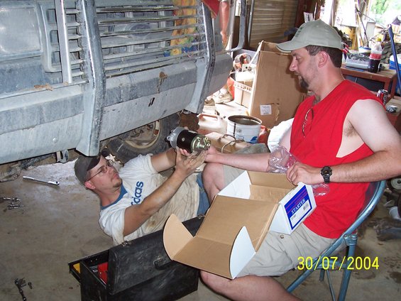 Mechanic installing starter motor on underside of vehicle. Box with 'STARTER' label visible