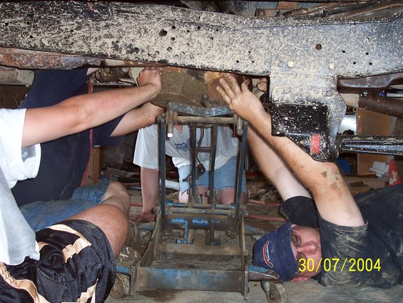 Underneath a vehicle with people working on the frame and suspension