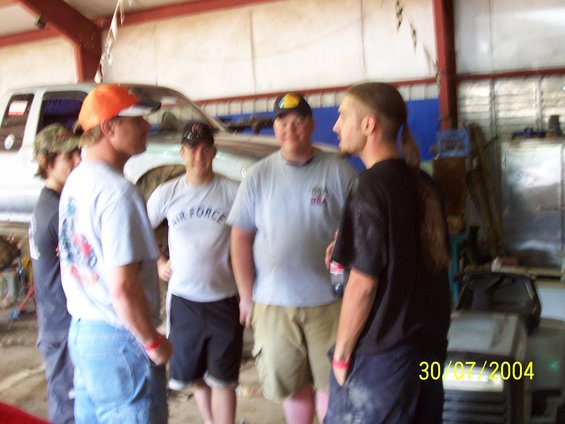 Men gathered in a garage with a truck in the background. Date stamp reads 30/07/2004