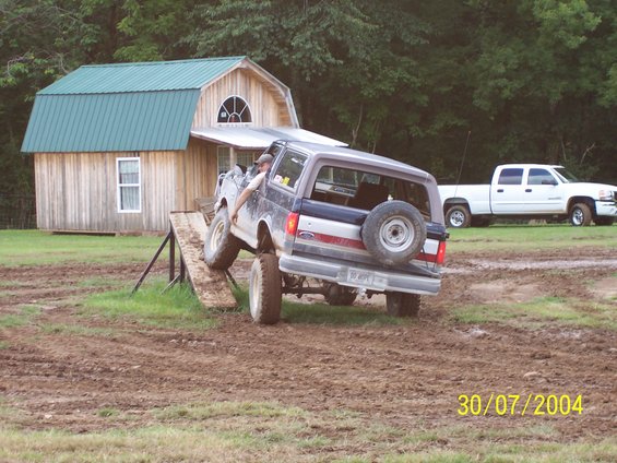 Dark blue Ford Bronco with a spare tire on the back, climbing a wooden ramp