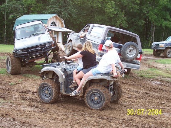 People on an ATV in mud, with several off-road vehicles around them