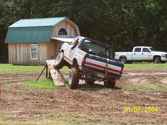 White Ford Bronco with blue and red stripe on rear, climbing a wooden ramp
