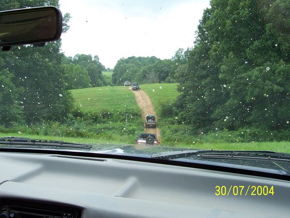 1979 Ford F-150 driving on a dirt road, rear view. The truck has a spare tire mounted on the tailgate