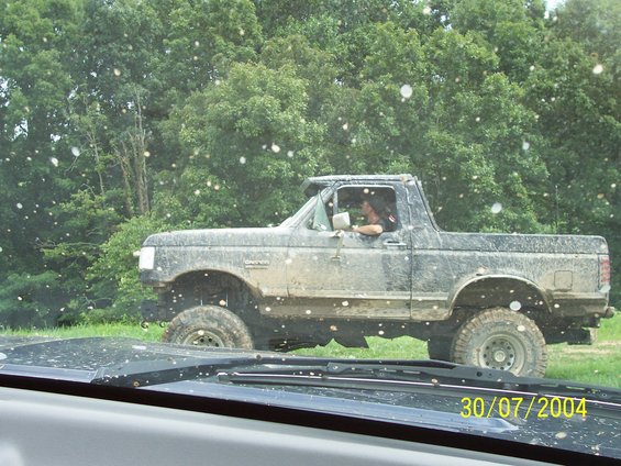 Muddy lifted pickup truck with a person driving, side view. Date stamp 30/07/2004