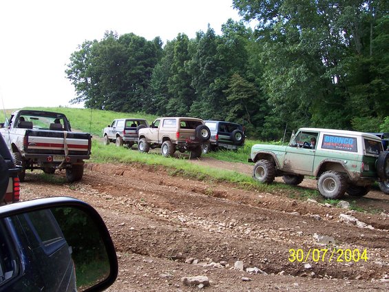 Green Ford Bronco with 'Bronco Magazine' decal on side, parked on dirt track with other off-road vehicles