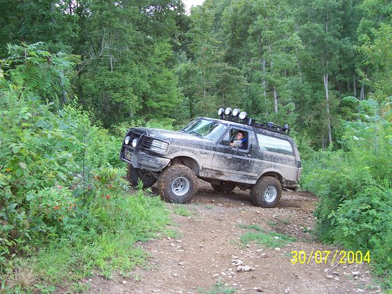 Black Ford Bronco with off-road tires and a brush guard driving on a dirt path