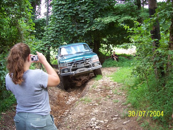 Green Ford Bronco navigating a rutted dirt trail with a woman taking a photo