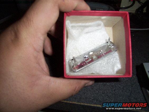 Chrome car emblem with red accents, held in a red box lined with white foam