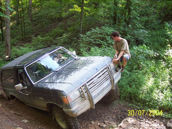 Black Ford Bronco with a brush guard stuck in mud on a wooded trail