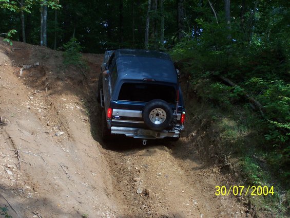 Dark blue SUV, possibly a Ford Bronco, on a dirt trail. Spare tire mounted on the rear door. Visible date stamp '30/07/2004'