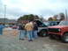 1984 Ford Bronco - Several men are gathered in a parking lot, observing two trucks, one with its hood open.