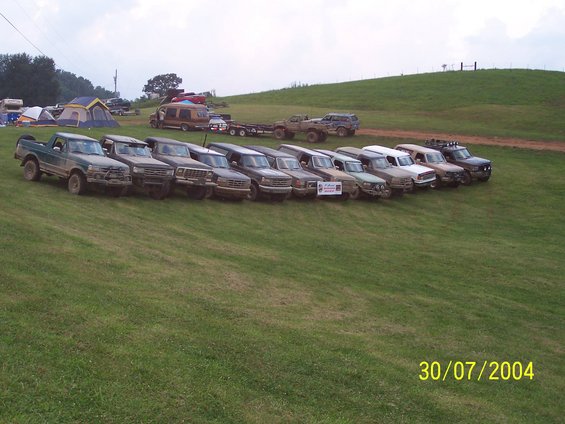 Line of pickup trucks and SUVs parked on a grassy hill, with tents and a van in the background. Date stamp reads 30/07/2004