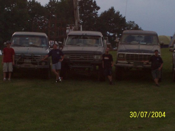 Three trucks parked in a grassy field with two people standing in front of them
