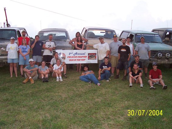 Group of people posing in front of several trucks and SUVs at an event