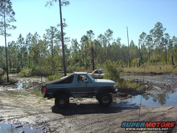 1993 Ford Bronco driving through muddy terrain with another vehicle in the background