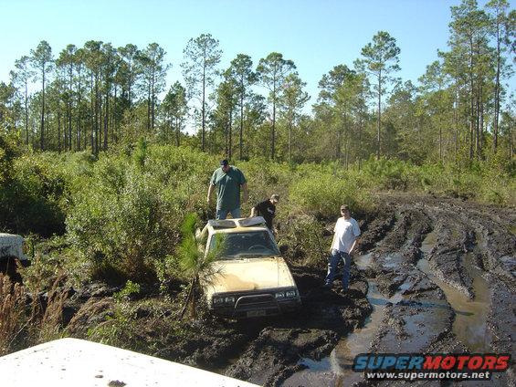 Yellow off-road vehicle stuck in deep mud with three people nearby