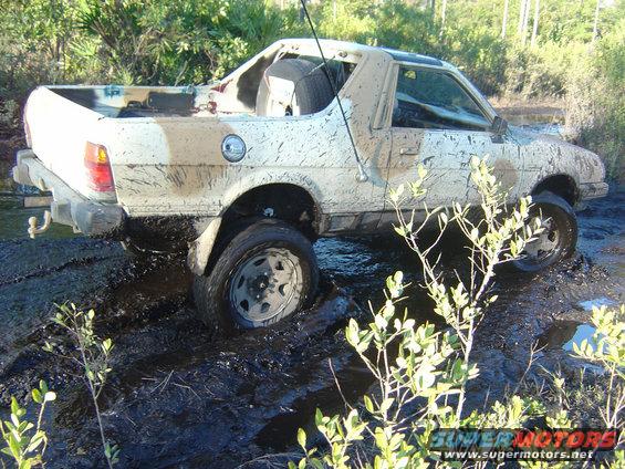 Mud-covered white pickup truck stuck in mud, rear quarter view