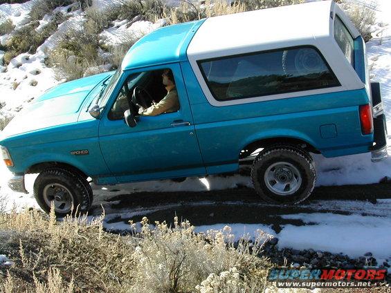 1994 Ford Bronco driving on a snowy dirt road, driver visible