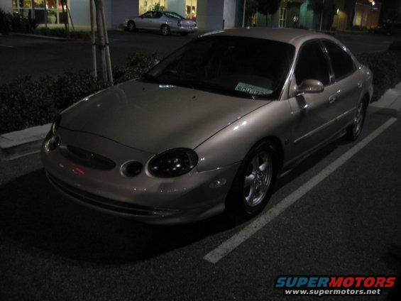 Tan sedan parked at night. Another silver car is in the background