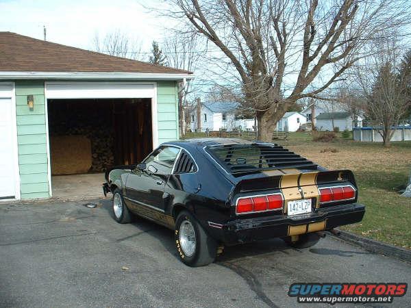 Black 1978 Ford Mustang II with gold stripes parked in driveway next to garage