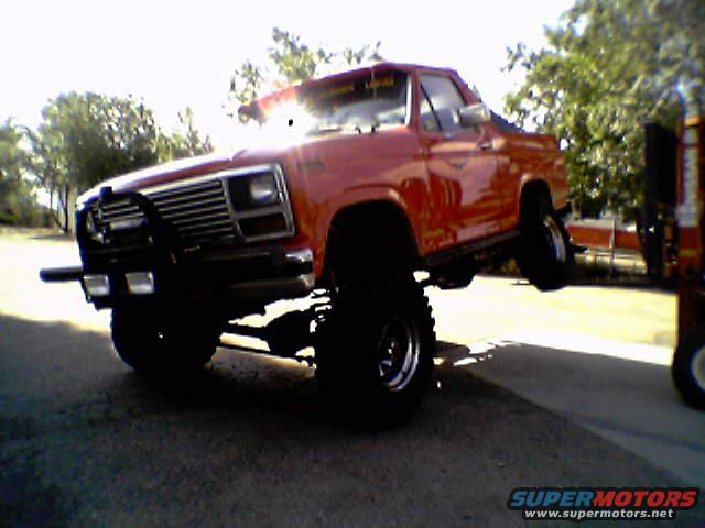 red lifted pickup truck with large tires and brush guard, front passenger side wheel in air