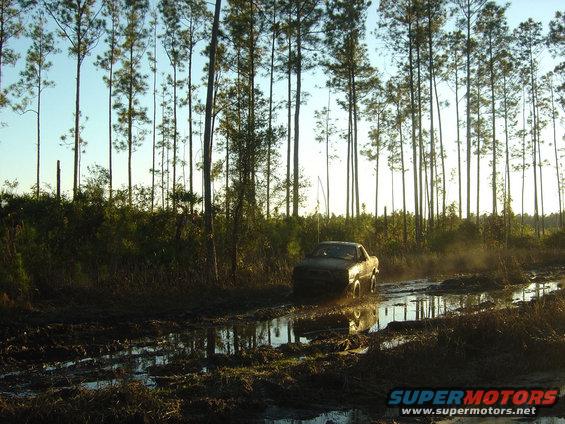 Vehicle driving through a muddy track with trees in the background