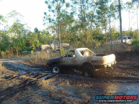 Several muddy trucks stuck in a wooded area with tire tracks in the mud