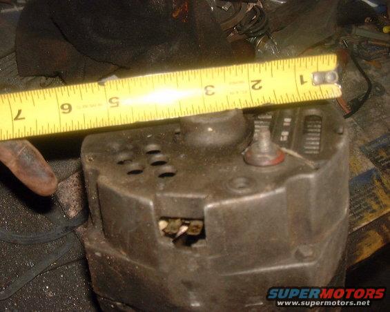 Alternator with yellow measuring tape across top. Some dust and wear visible