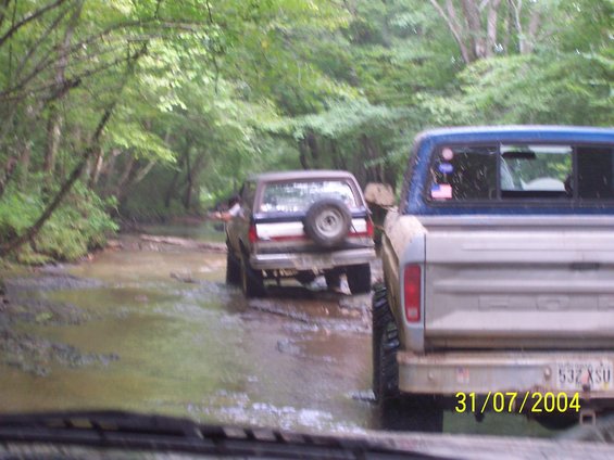 Rear view of a blue and silver pickup truck driving through water, with another SUV behind it