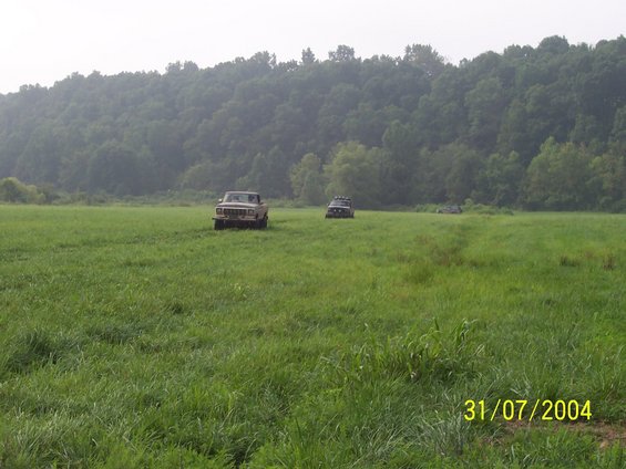 Two trucks parked in a grassy field with trees in the background. Date stamp reads 31/07/2004