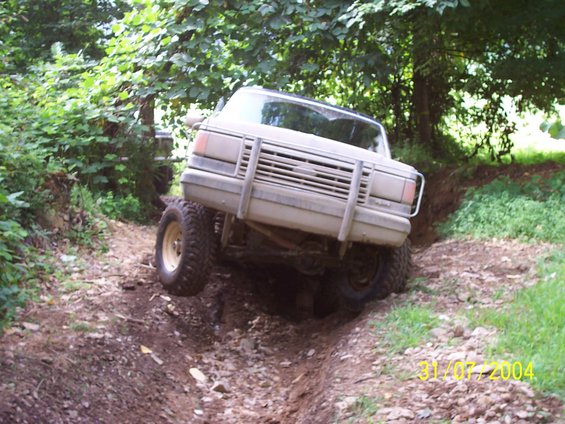 Tan truck with a large grille guard navigating a ditch, front left wheel off the ground