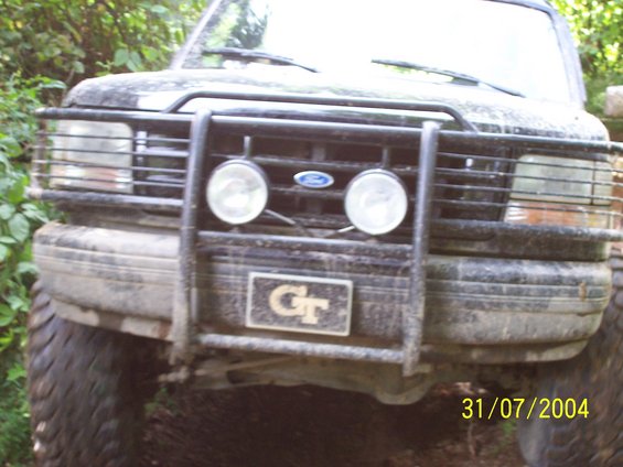Front view of a dirty Ford truck with a brush guard and two round lights. A GT license plate is attached to the guard