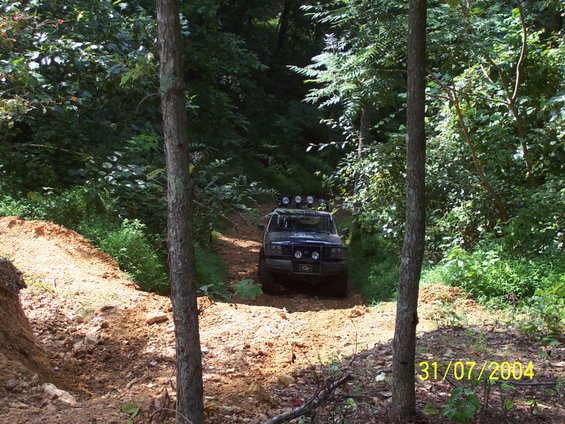 Off-road vehicle with roof lights driving on a dirt path through trees