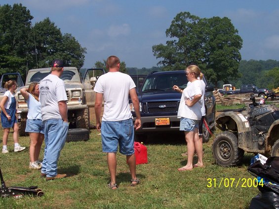 People standing around a blue Ford Explorer and an older, lifted Ford truck. An ATV is parked nearby