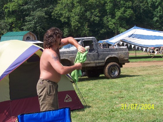 Mud-splattered dark gray 1984 Ford Bronco II, 3/4 front view, with a man cleaning the driver's side window