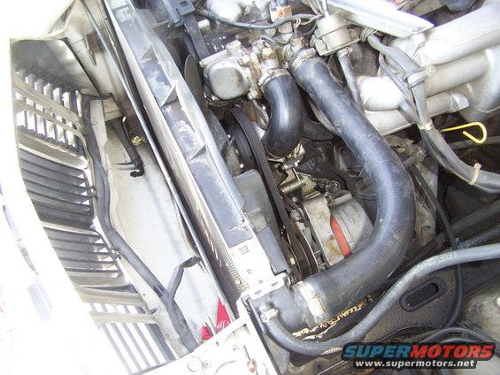 Engine bay with radiator, hoses, and belts visible. Some dirt and debris present