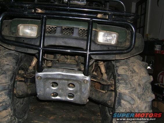 Front view of a green ATV with a black brush guard and skid plate