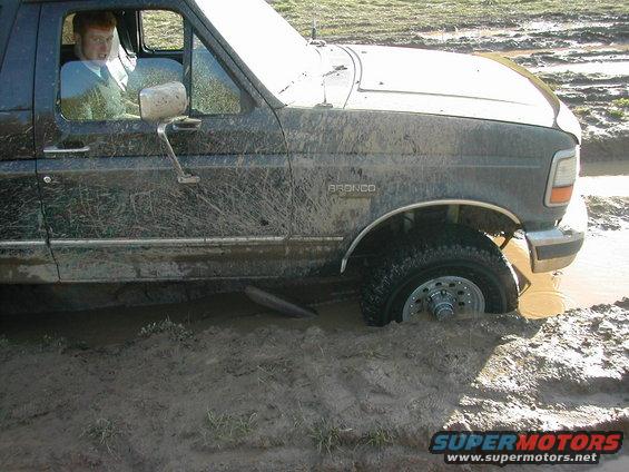 Muddy 1992 Ford Bronco stuck in mud, driver visible