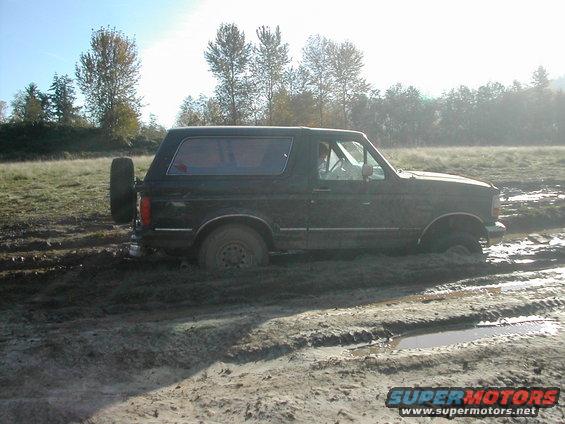 Dark Ford Bronco stuck in deep mud, spare tire mounted on back