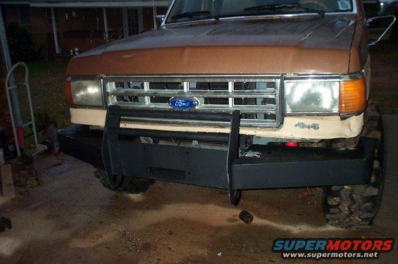 Brown 1987 Ford Bronco front end with a black bull bar and winch, tan grille, and chrome headlights