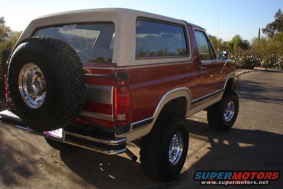 Red and tan Ford Bronco with a spare tire on the back, lifted with large tires